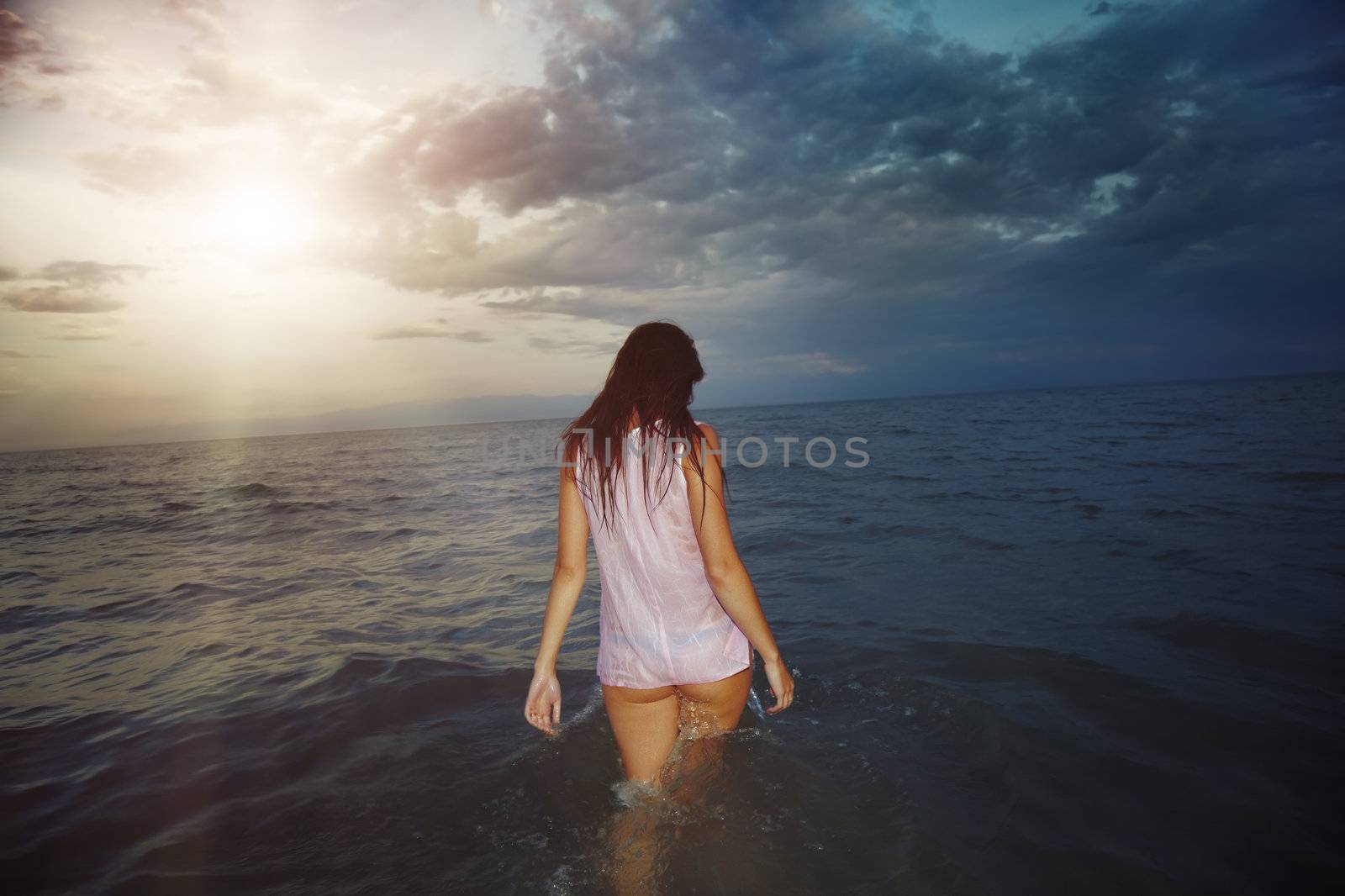 Woman in the sea walking to the sun