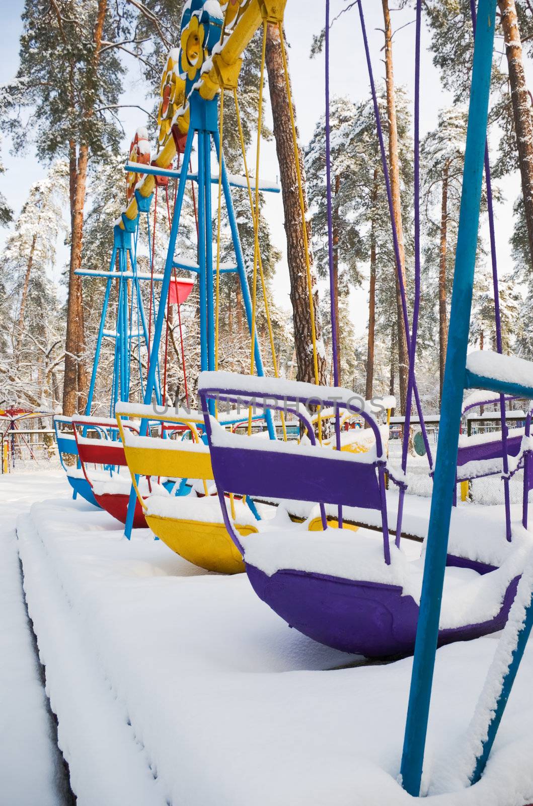 Child's swings in an empty park playground covered in snow.