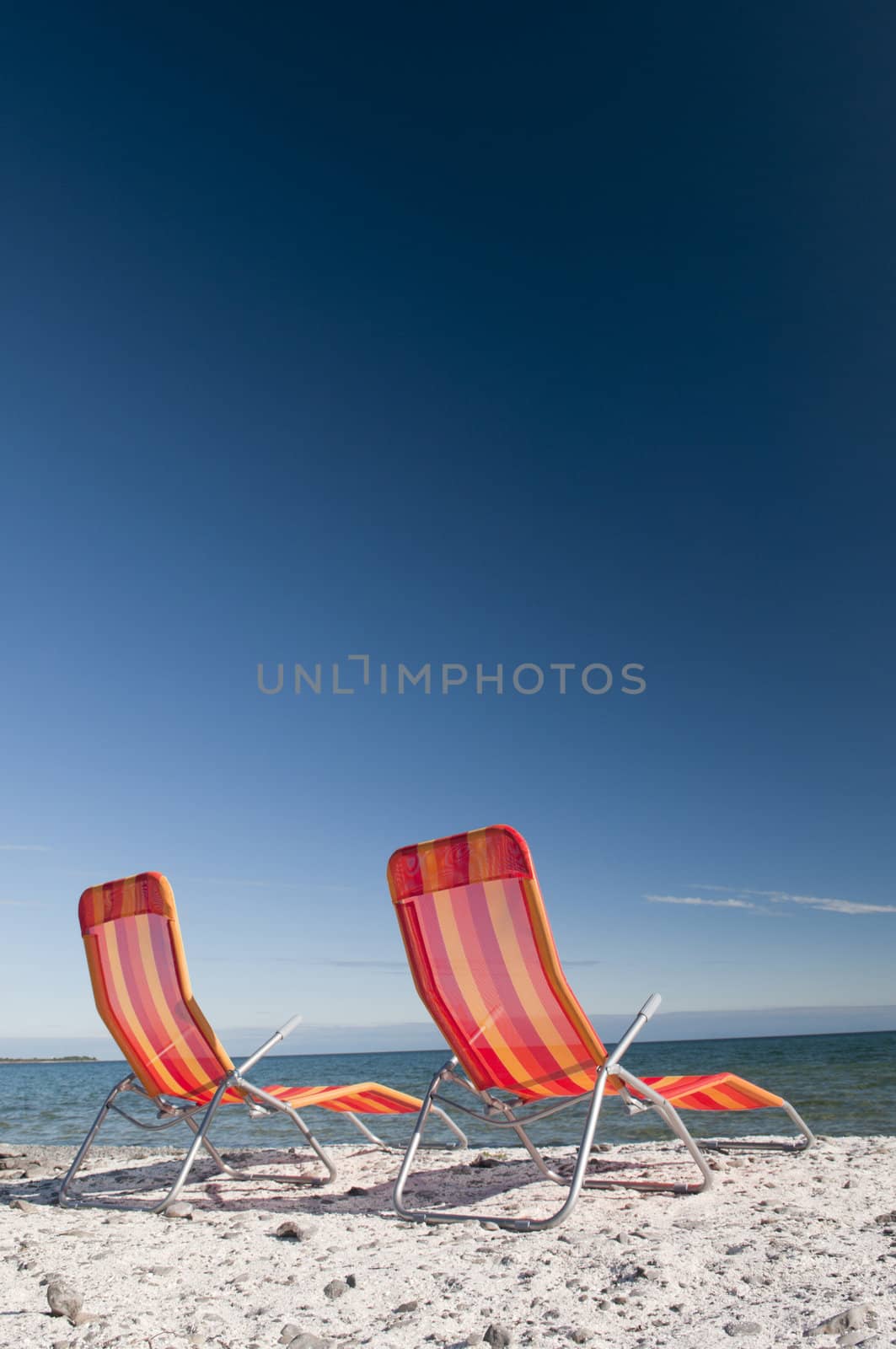 Lounging beach chairs on the Lake Ontario shoreline with large copy space area in the deep blue sky