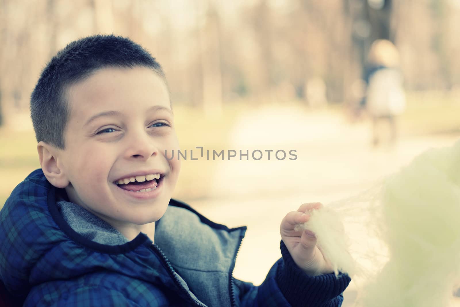 Happy young boy eating sugarwool in a park