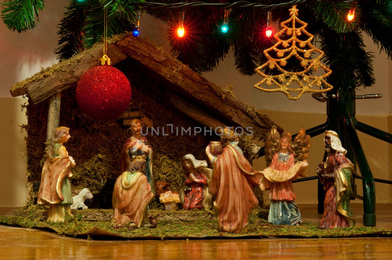 christmas nativity scene with hand-colored ceramic figures and below tree with many decorations (lights, bauble and star)