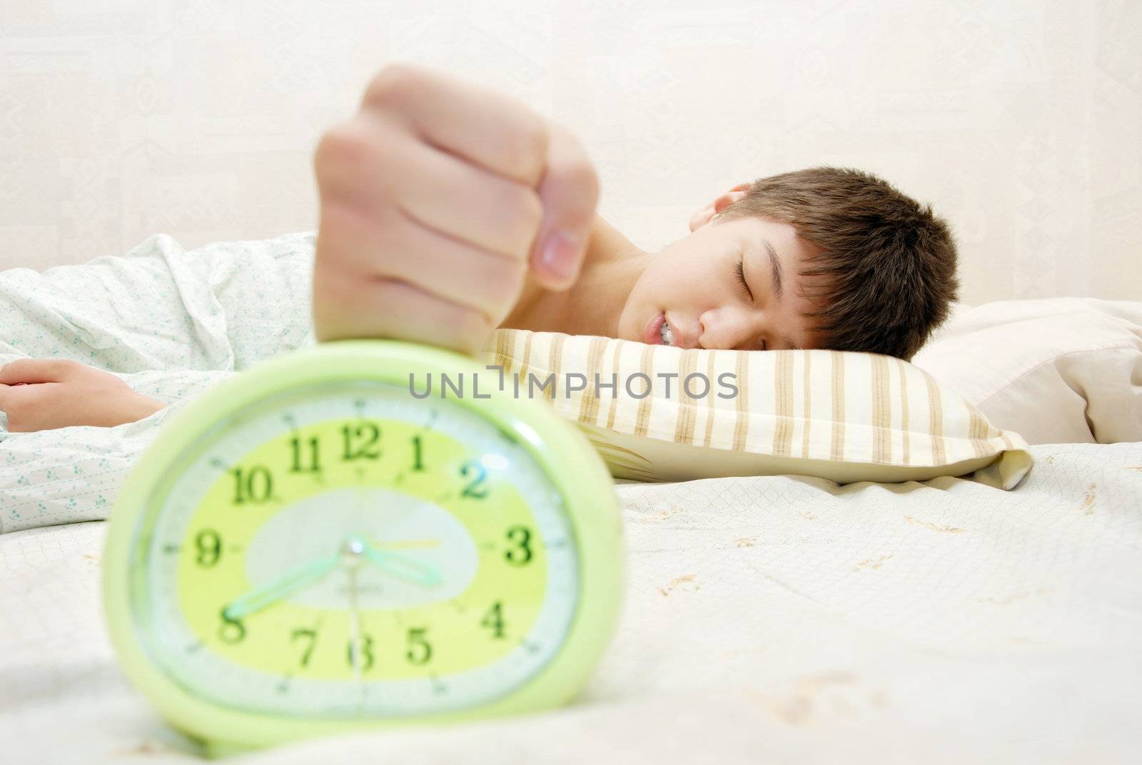 Sleeping boy hitting the alarm clock at the early morning