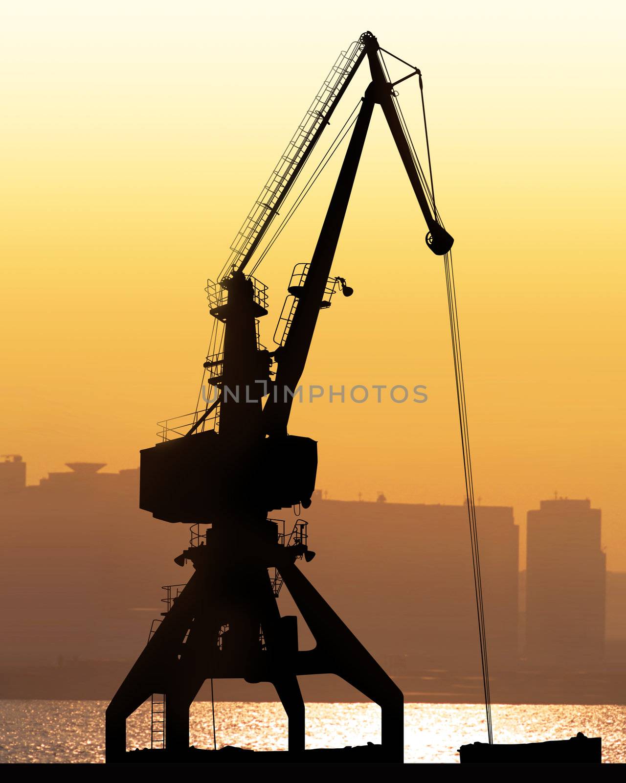 crane sit dramatically against a colorful sunset in a large shipyard