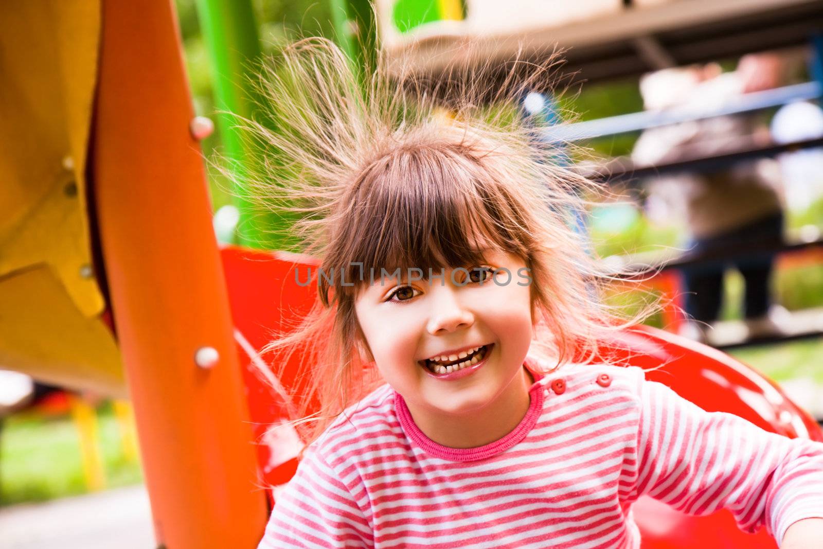 Sweet little girl on playground with electric hair smiling at camera