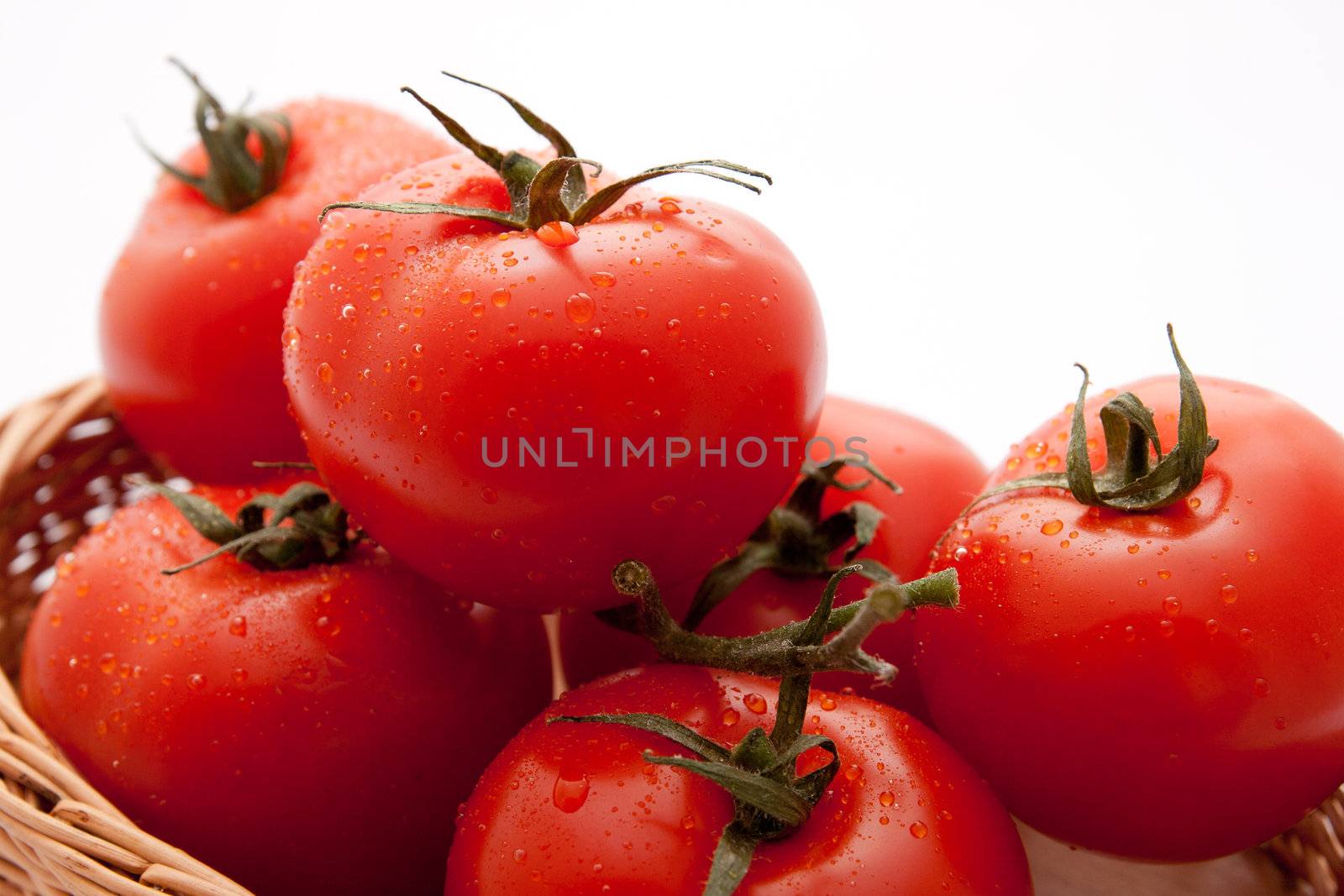 Fresh tomatoes in a wicker basket on white background