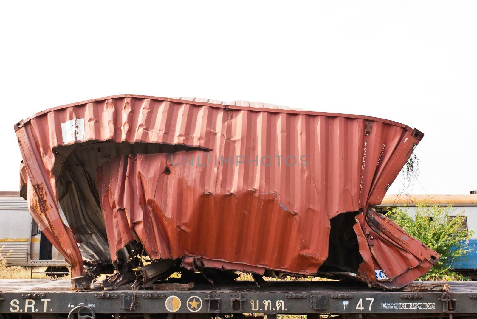 A wrackage of red steel container taken from train yard on a sunny day
