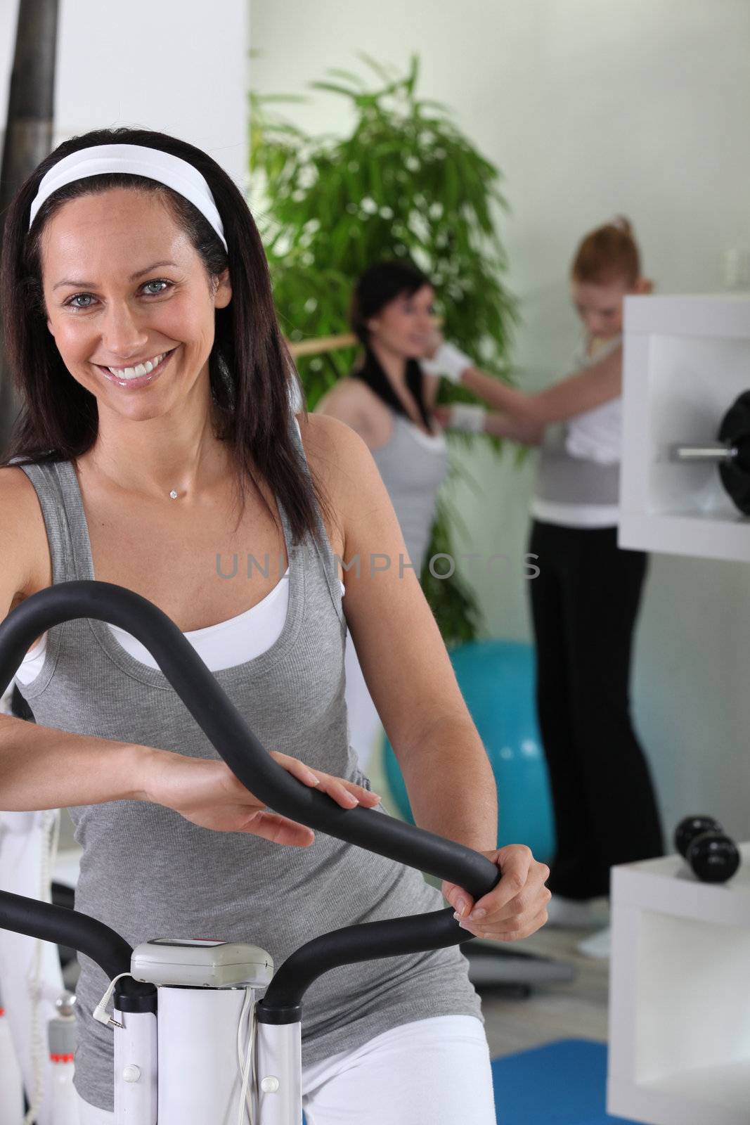 Smiling brown-haired woman on cross trainer by phovoir