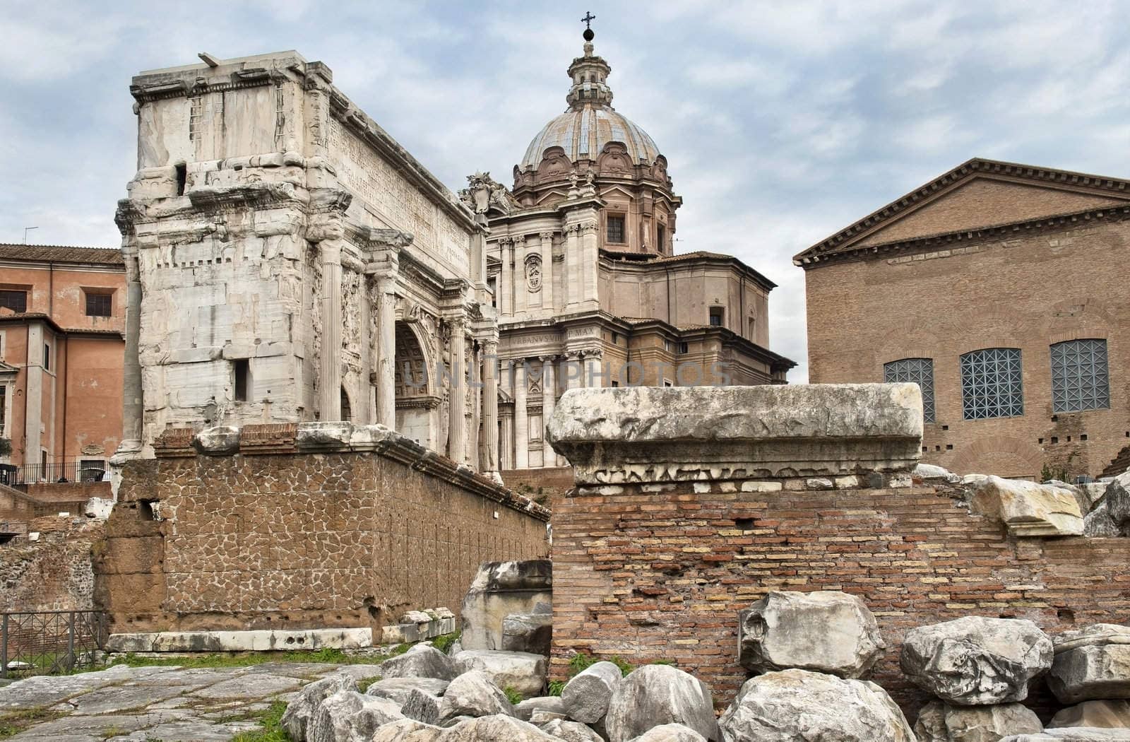 ruins of the Roman Forum, a triumphal arch and the Catholic church against cloudy sky