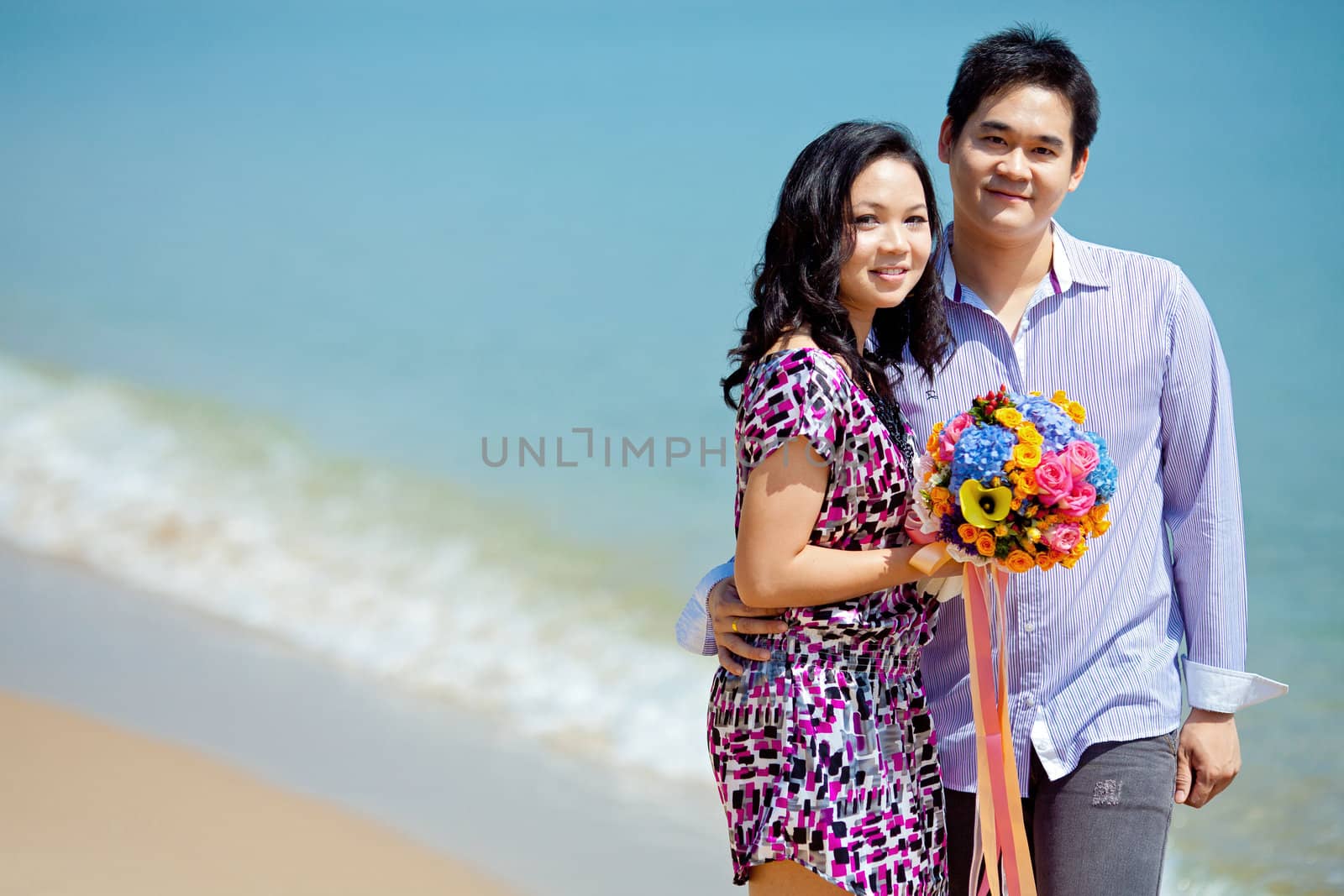 attractive couple standing together in the beach with beautiful bouquet