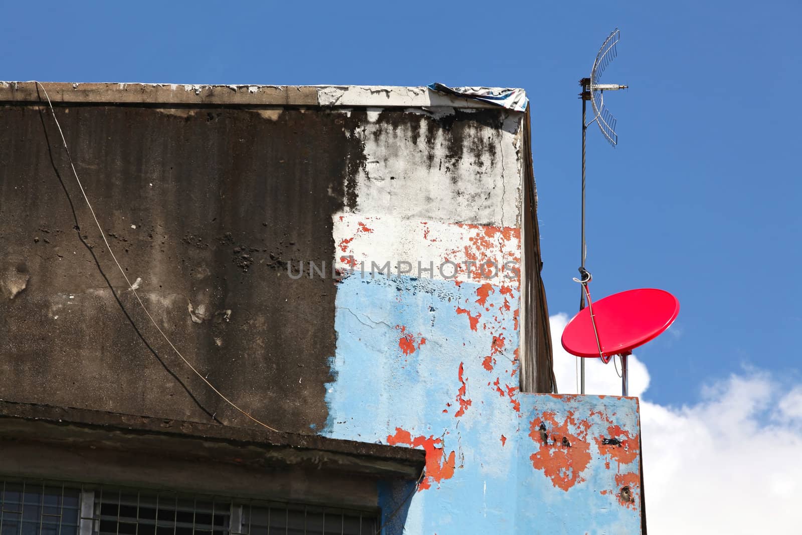 red satellite dish with cracking building on sunny blue sky