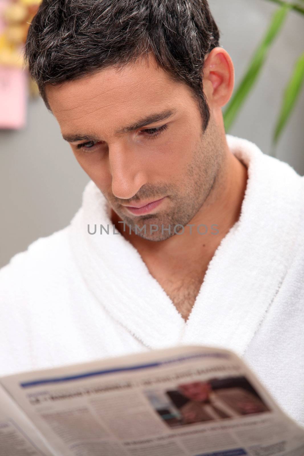 Handsome man in a toweling robe reading a journal by phovoir