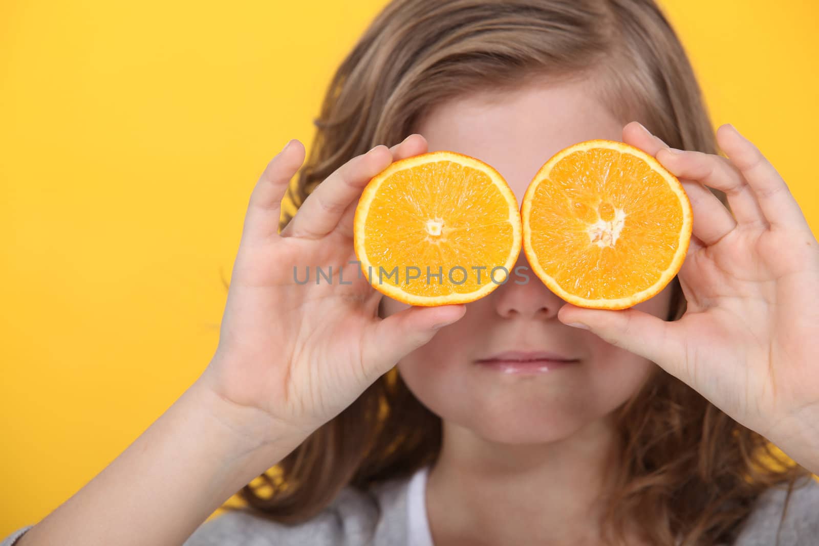 Little girl covering eyes with slices of orange