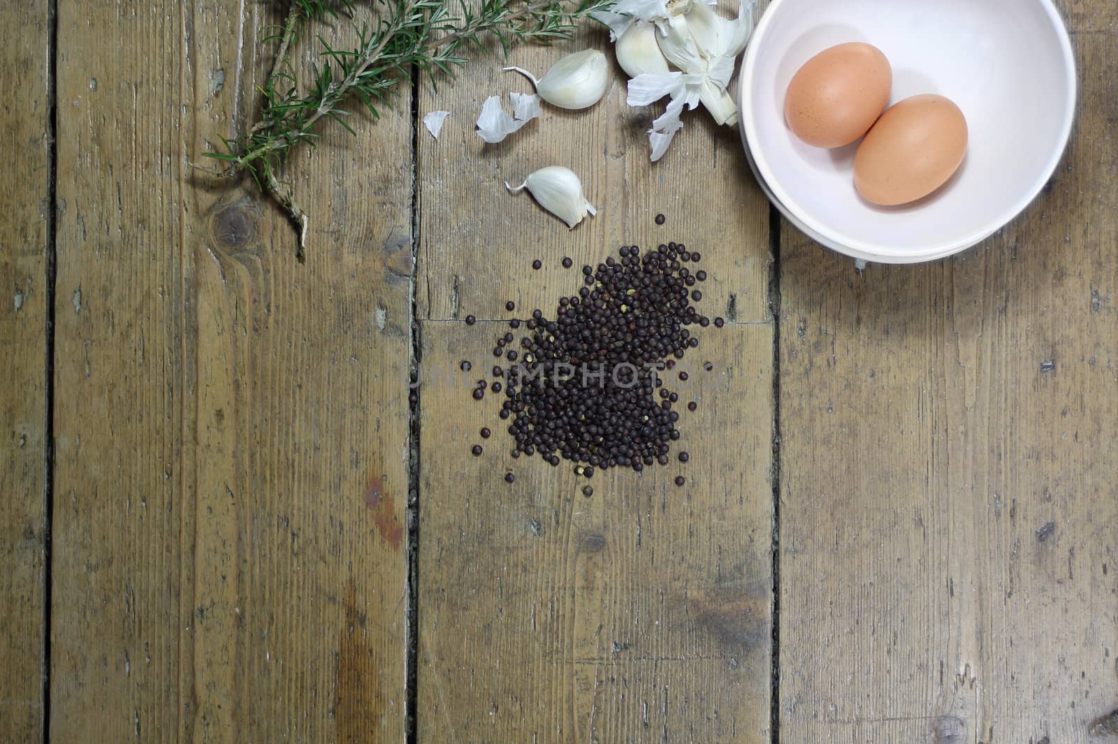 Kitchen ingredients comprising of brown eggs, garlic, fresh rosemary and black lentils. All set on a landscape format against a wooden background with plenty of copy-space available.