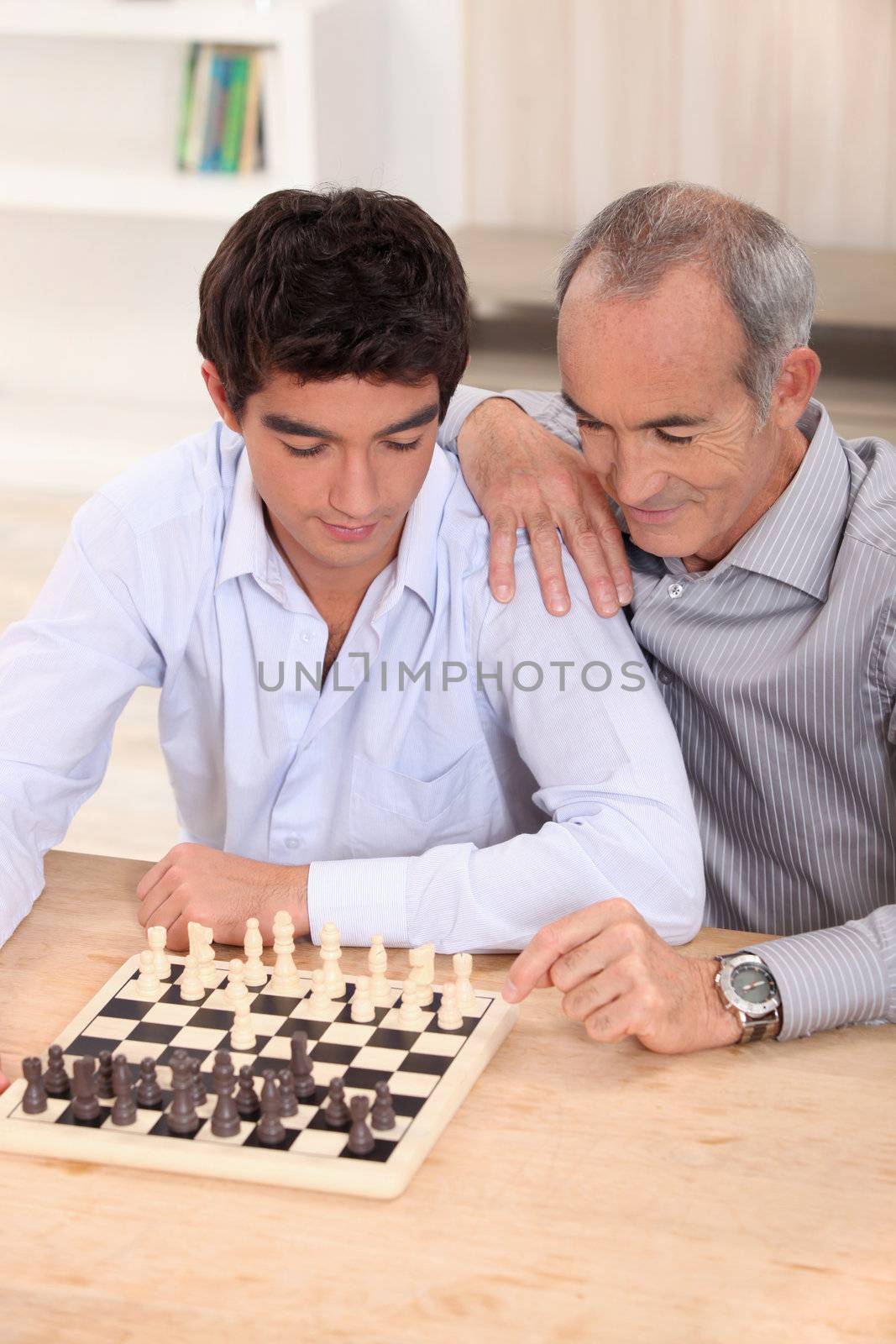 Father and son playing chess by phovoir
