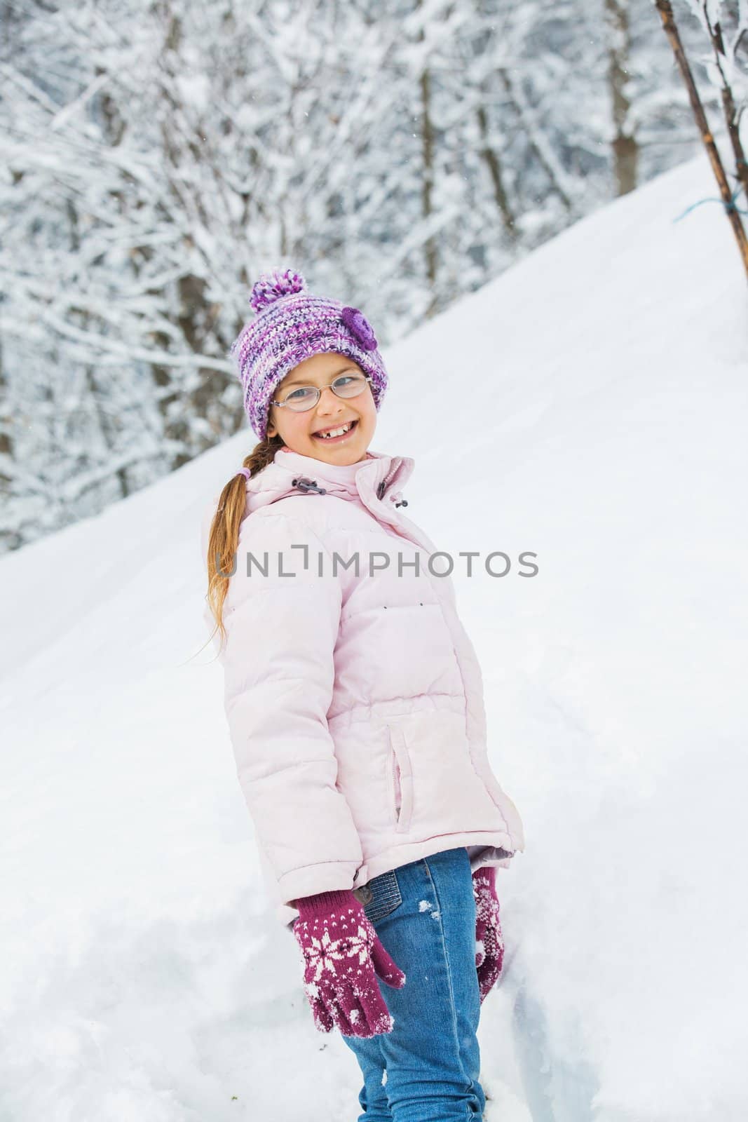 Smiling happy girl having fun outdoors on snowing winter day in Alps playing in snow. Vertical view