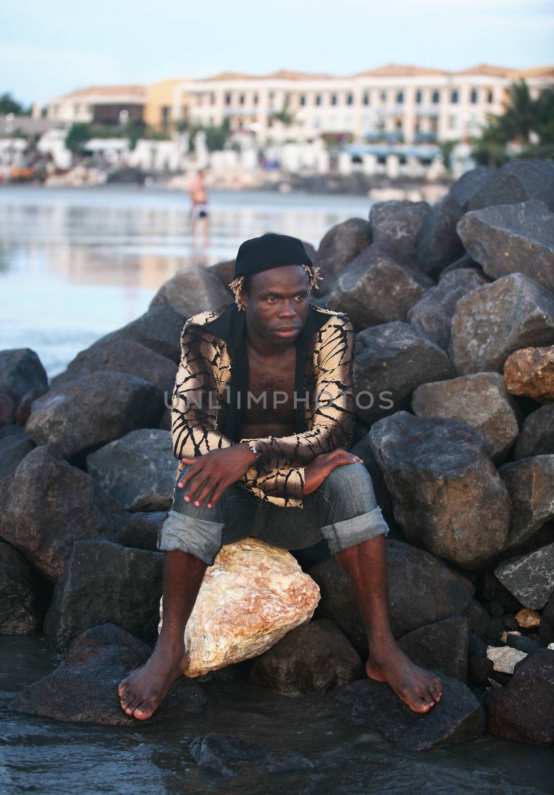 Portrait of the young African person sitting on stones at ocean. Bali. Indonesia