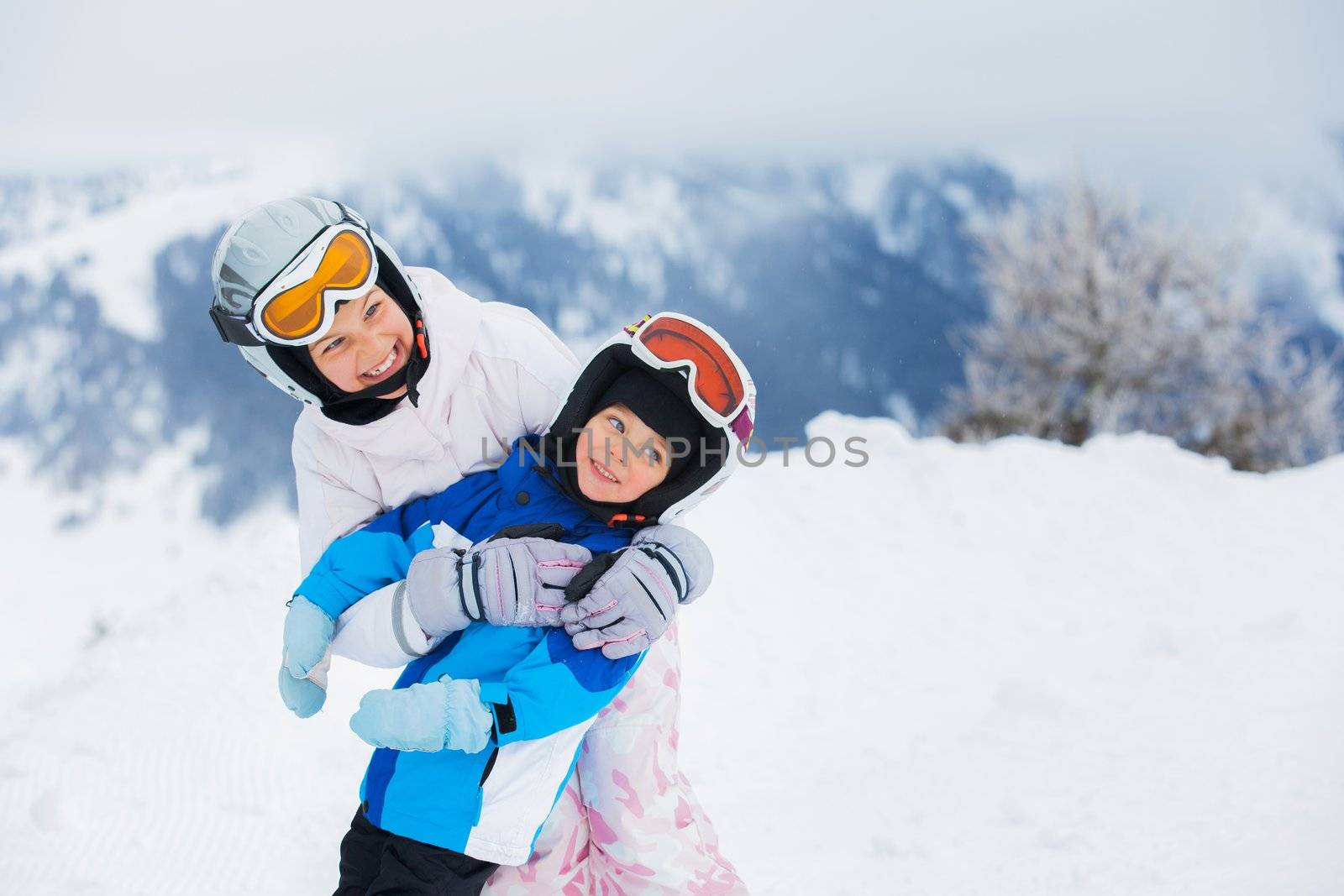 Happy brother and sister in ski goggles and helmets plaing on the downhill in wintertime