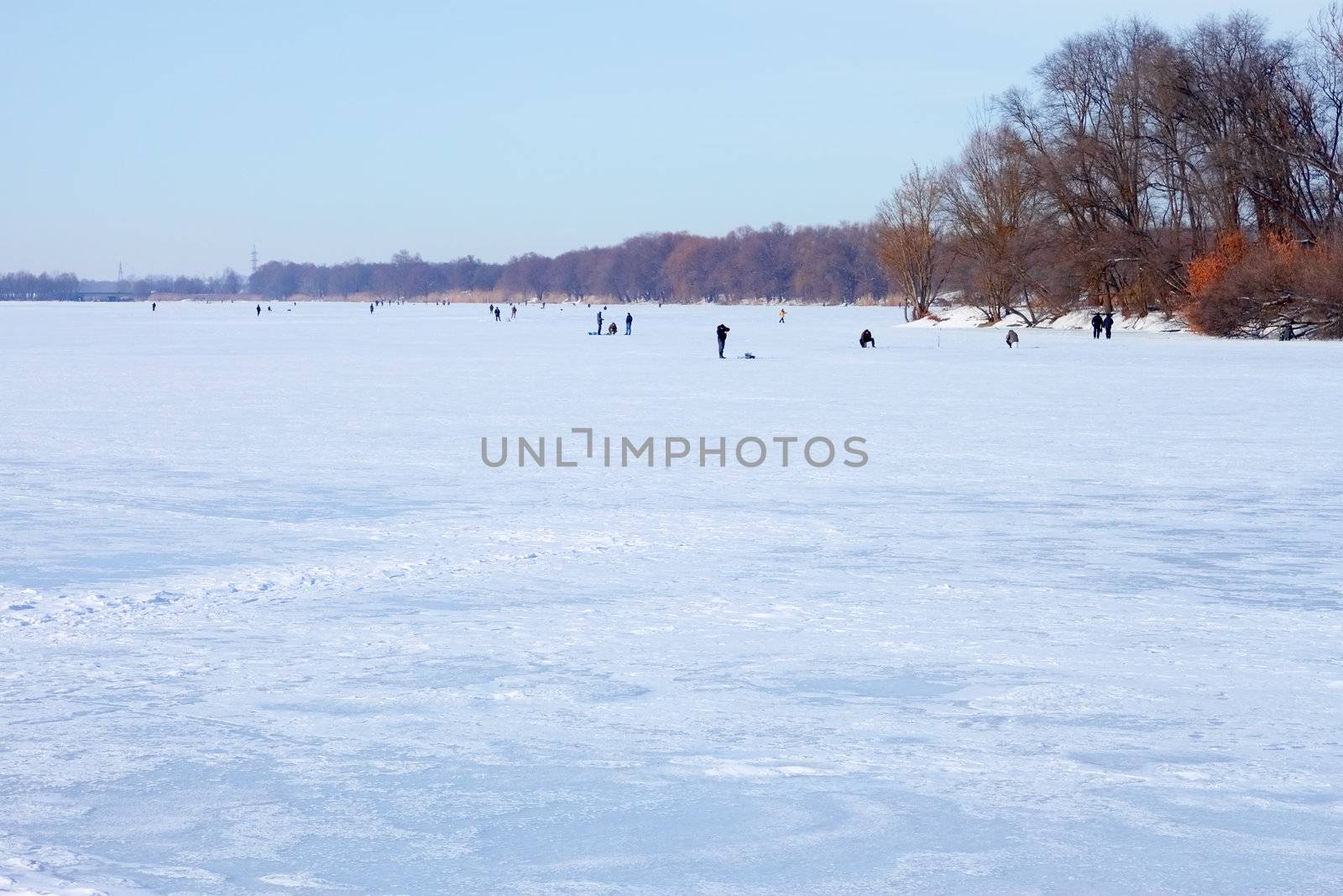 Winter scene. Snow hummocks on frozen reservoir. Fishermans catch fish in river on the ice surface