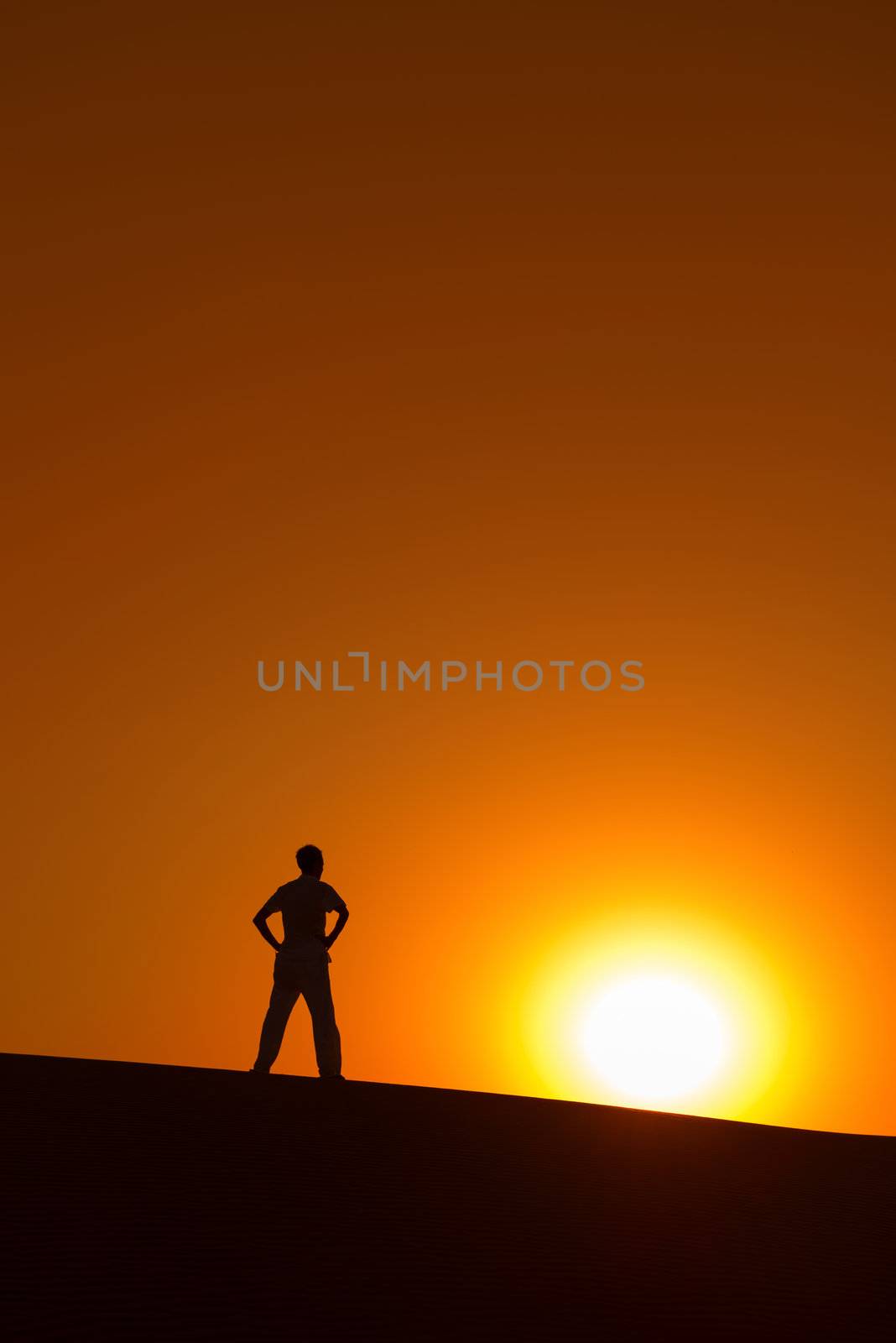 Man at orange background with big sun under horizon with heroic achievement gesture