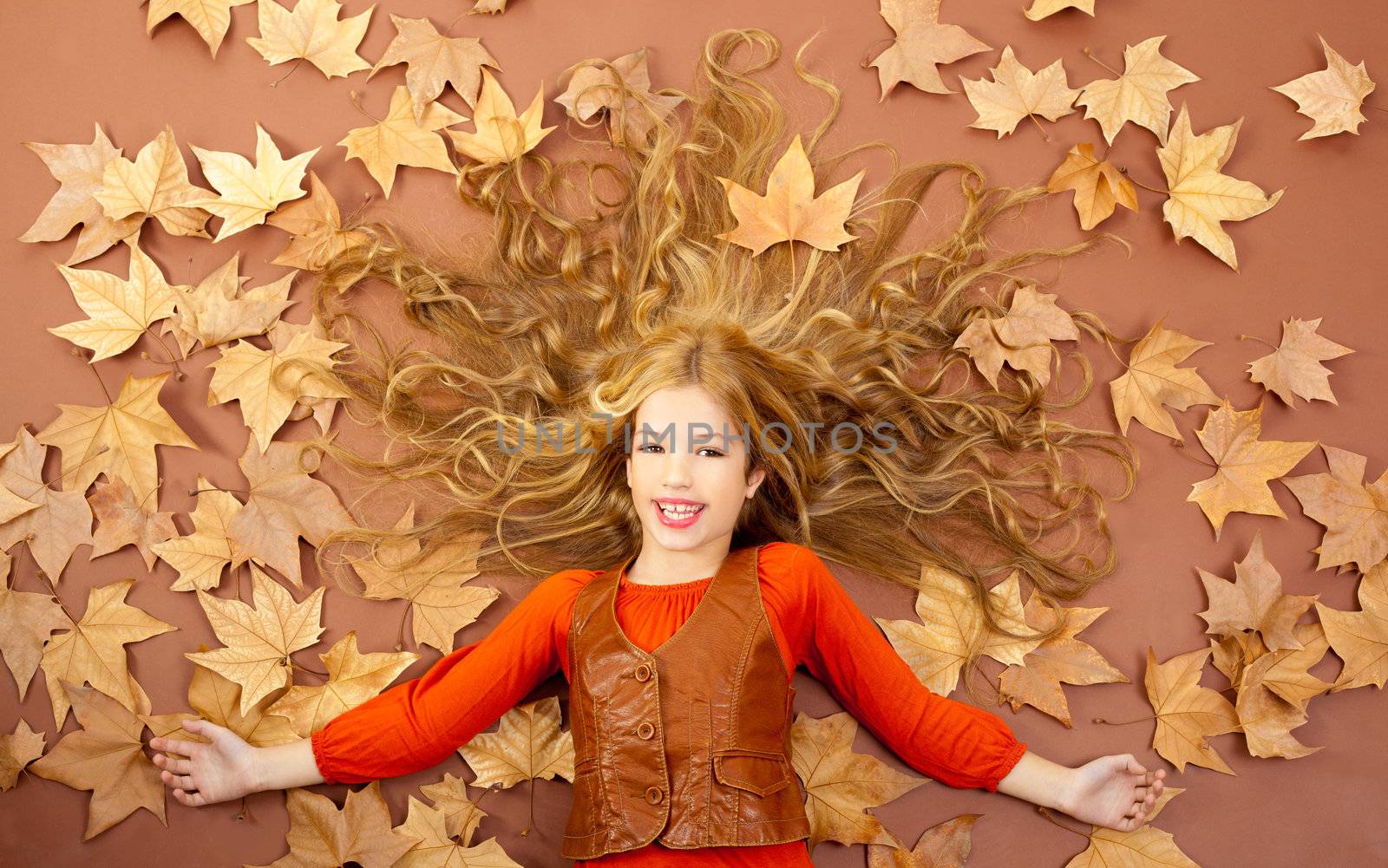 autumn fall little blond girl on dried tree leaves background and long spread hair