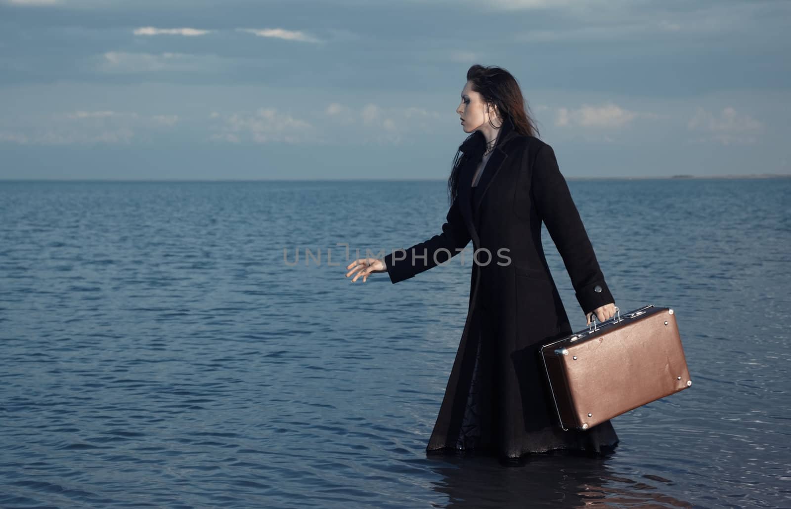 Woman in black coat going to the sea with luggage