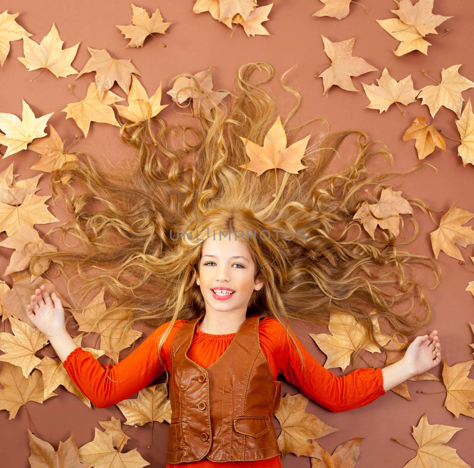 autumn fall little blond girl on dried tree leaves background and long spread hair