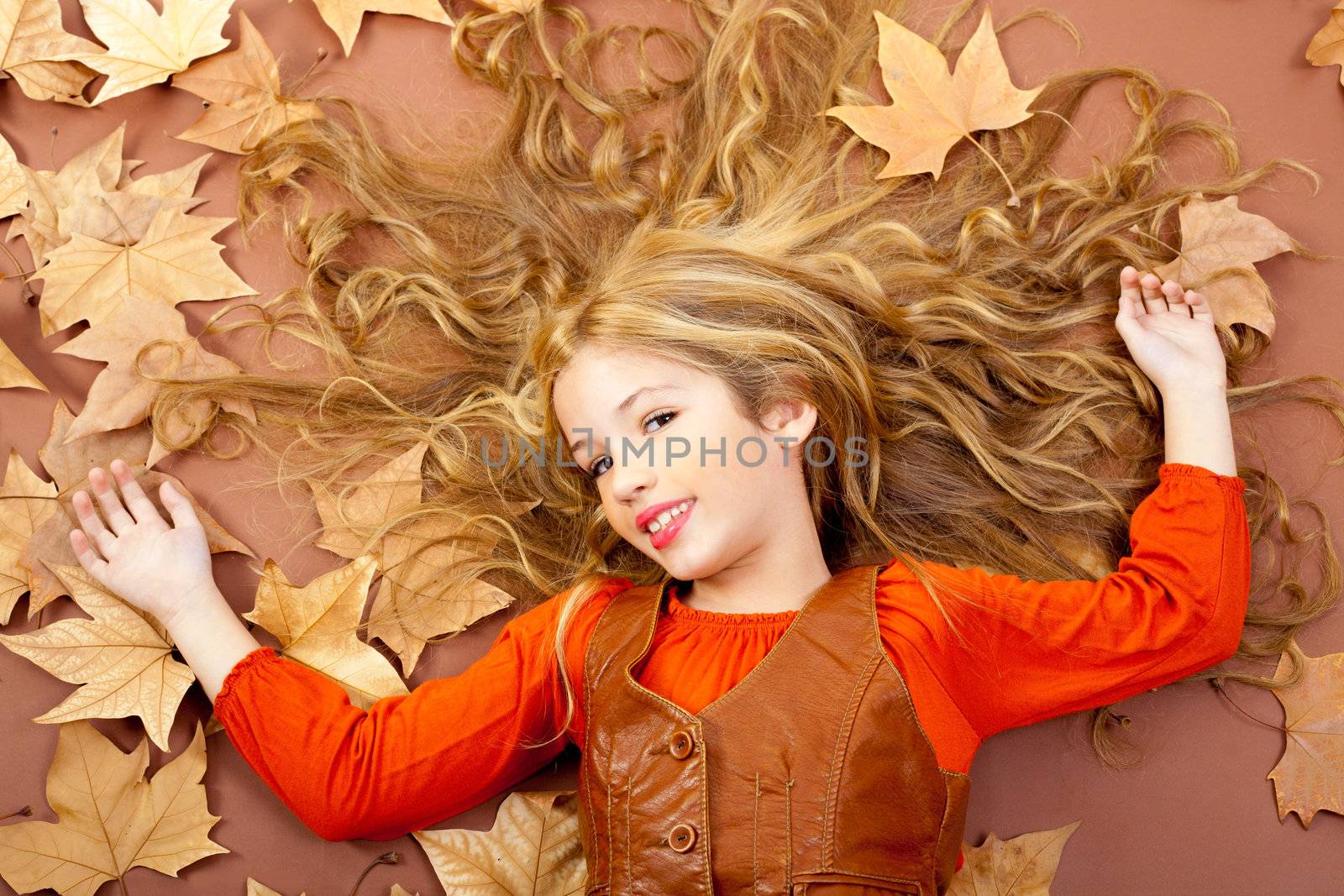 autumn fall little blond girl on dried tree leaves background and long spread hair