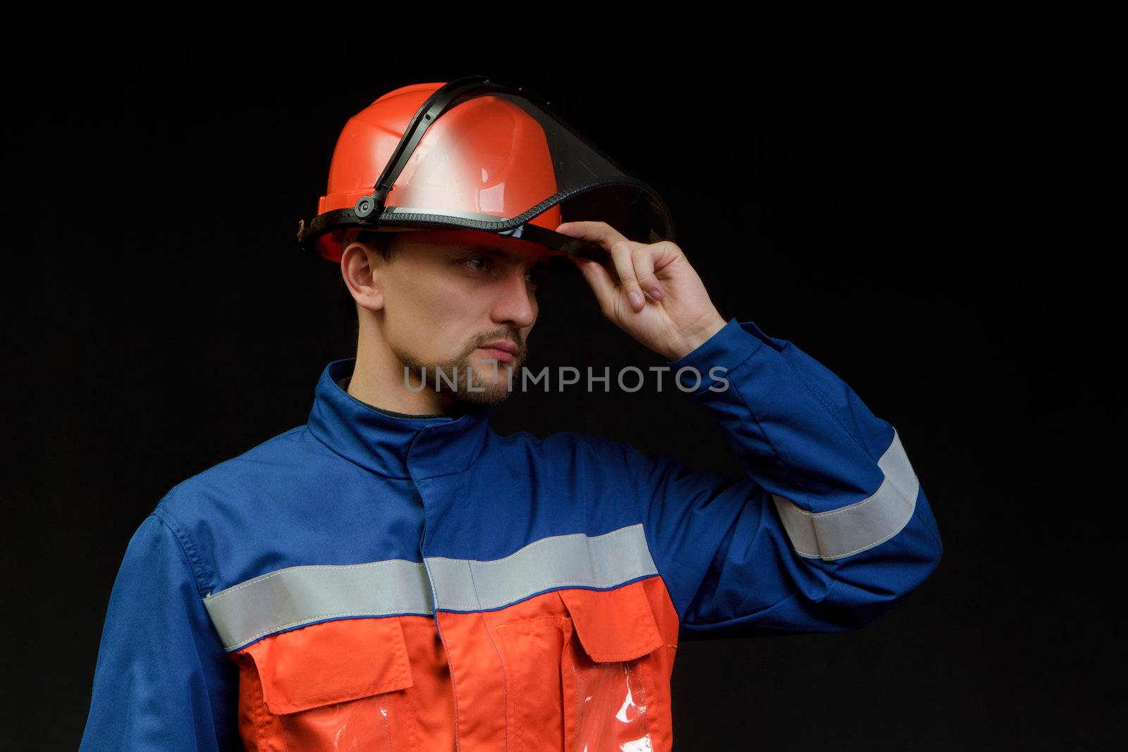 The worker in overalls and a helmet on a black background 