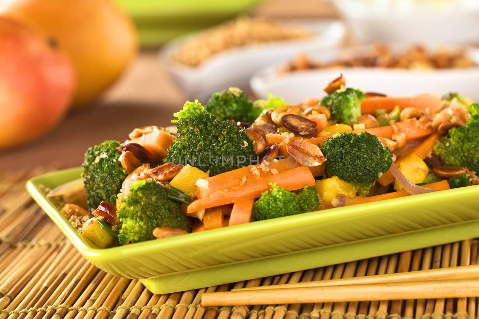 Vegetarian stir-fry Thai-style with broccoli, carrot, onion, mango with fried coconut flakes and peanuts (Selective Focus, Focus on the broccoli in the middle of the image)