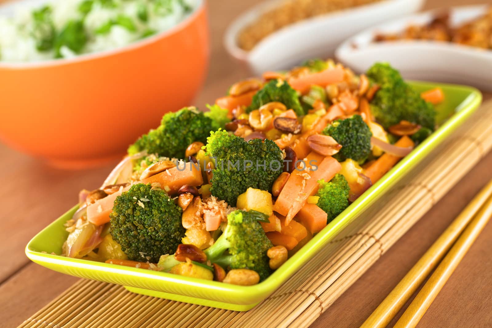 Vegetarian stir-fry Thai-style with broccoli, carrot, onion, mango with fried coconut flakes and peanuts (Selective Focus, Focus on the broccoli in the middle of the image)