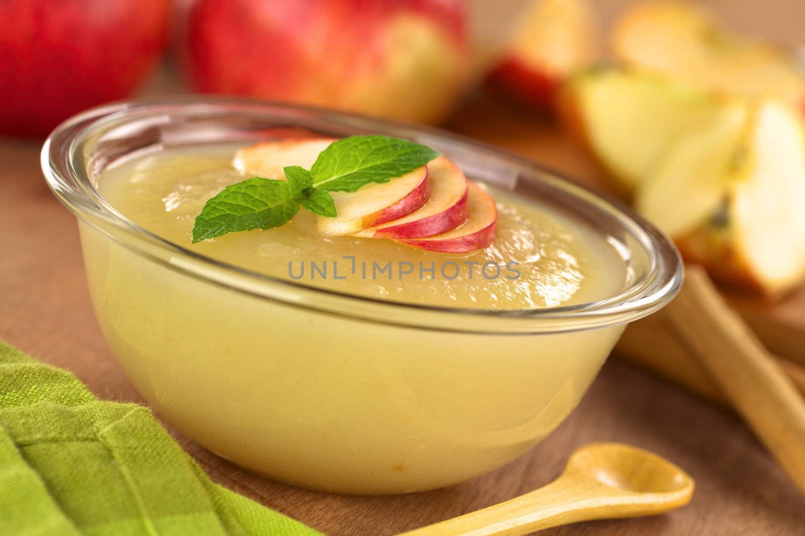 Fresh homemade apple sauce with apples in the back (Selective Focus, Focus on the front of the apple slices and the mint leaf on the sauce) 