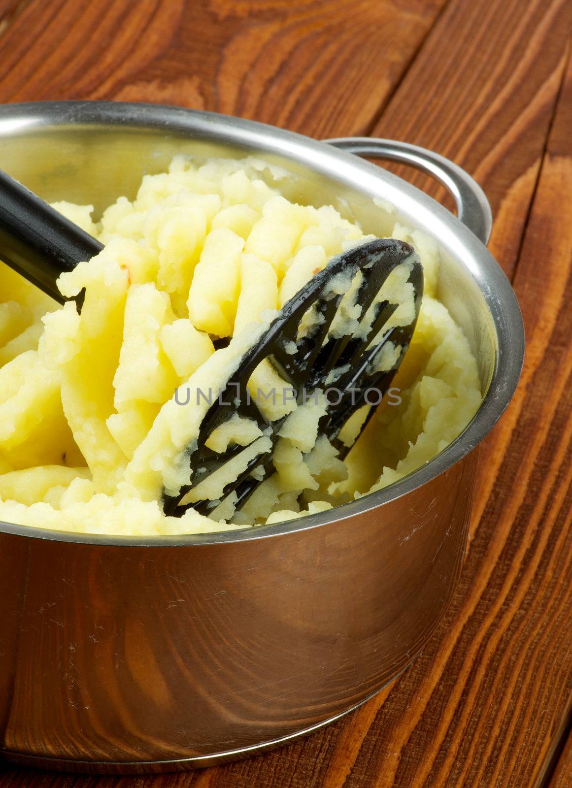 Preparing Mashed Potato in Stainless Steel Pan with Black Potato Masher on Wooden background