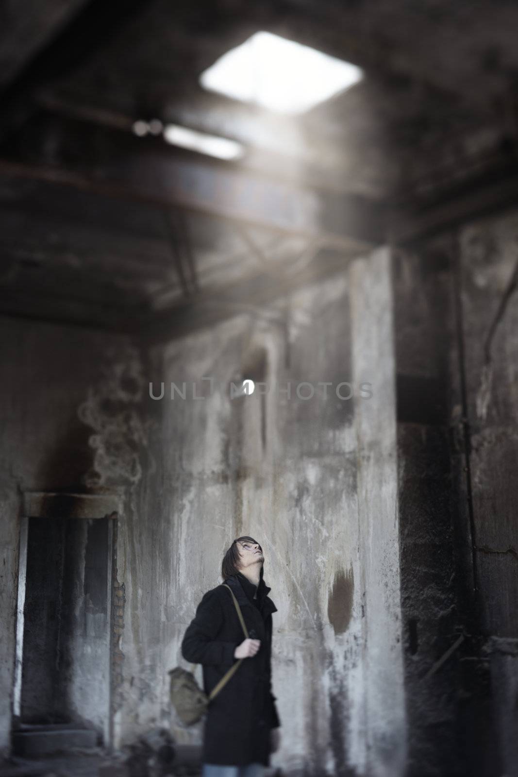 Alone explorer indoors looking up to the hole in the roof with sunbeam. Shallow depth of field due to the tilt lens for movie effect