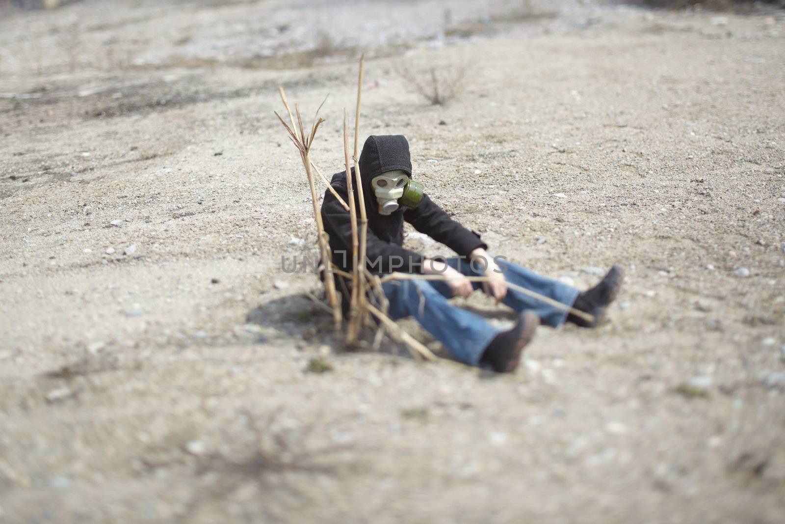 Single human in gas mask sitting in the desert near the dead plant. Concept of the futuristic environmental disaster. Special color added and shallow depth of field due to the tilt/shift lens for movie effect
