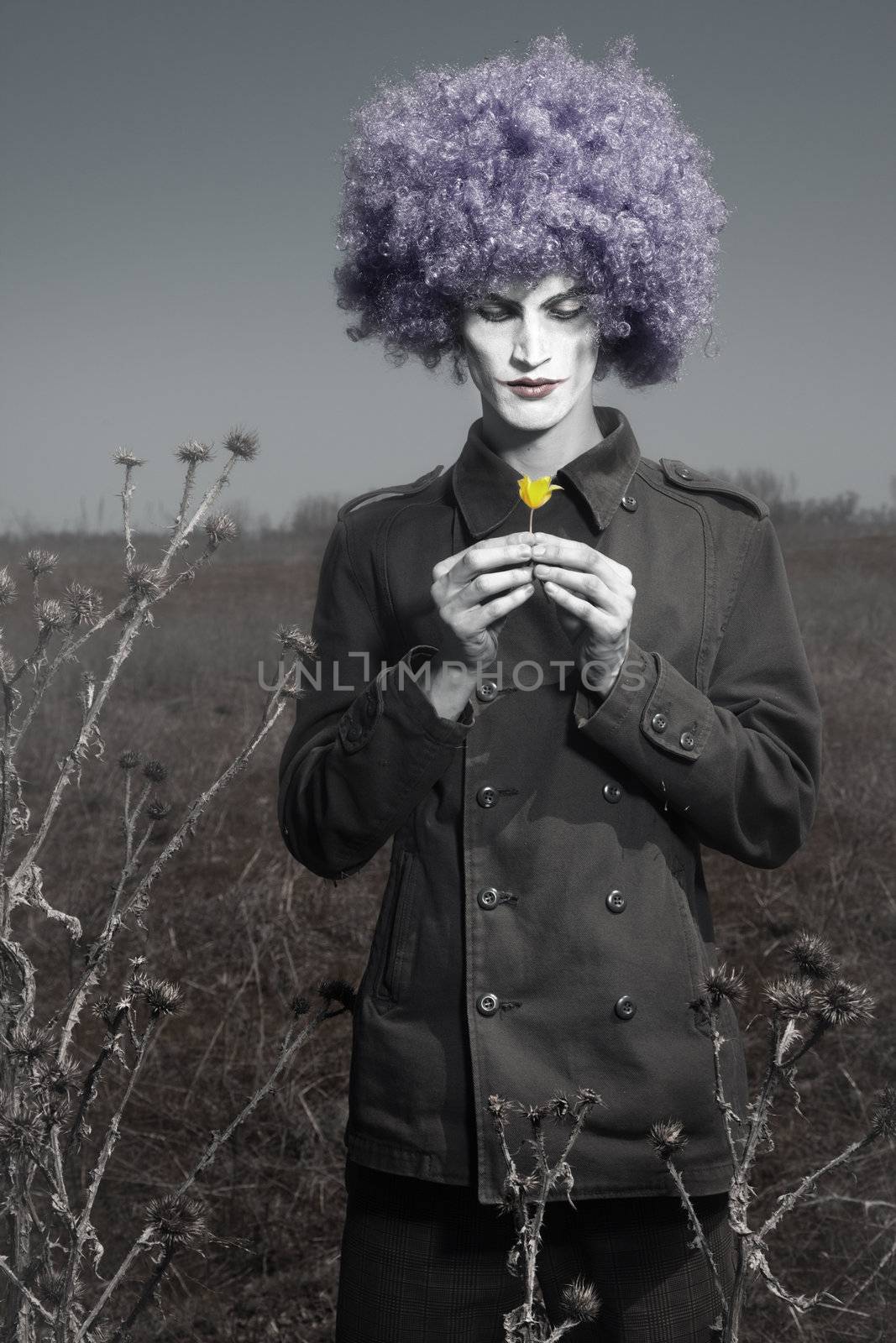 Romantic photo of the clown outdoors holding yellow flower