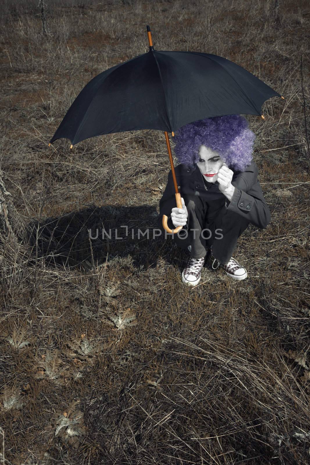 Alone funny man outdoors sitting and holding umbrella. Artistic color and darkness added