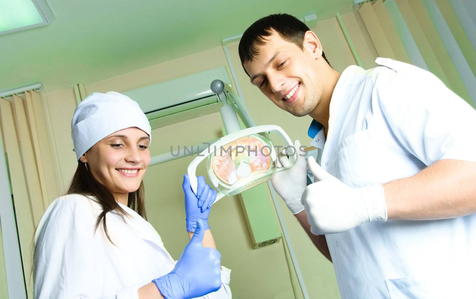 two young dentists satisfied with the result with their thumbs up looking at the patient