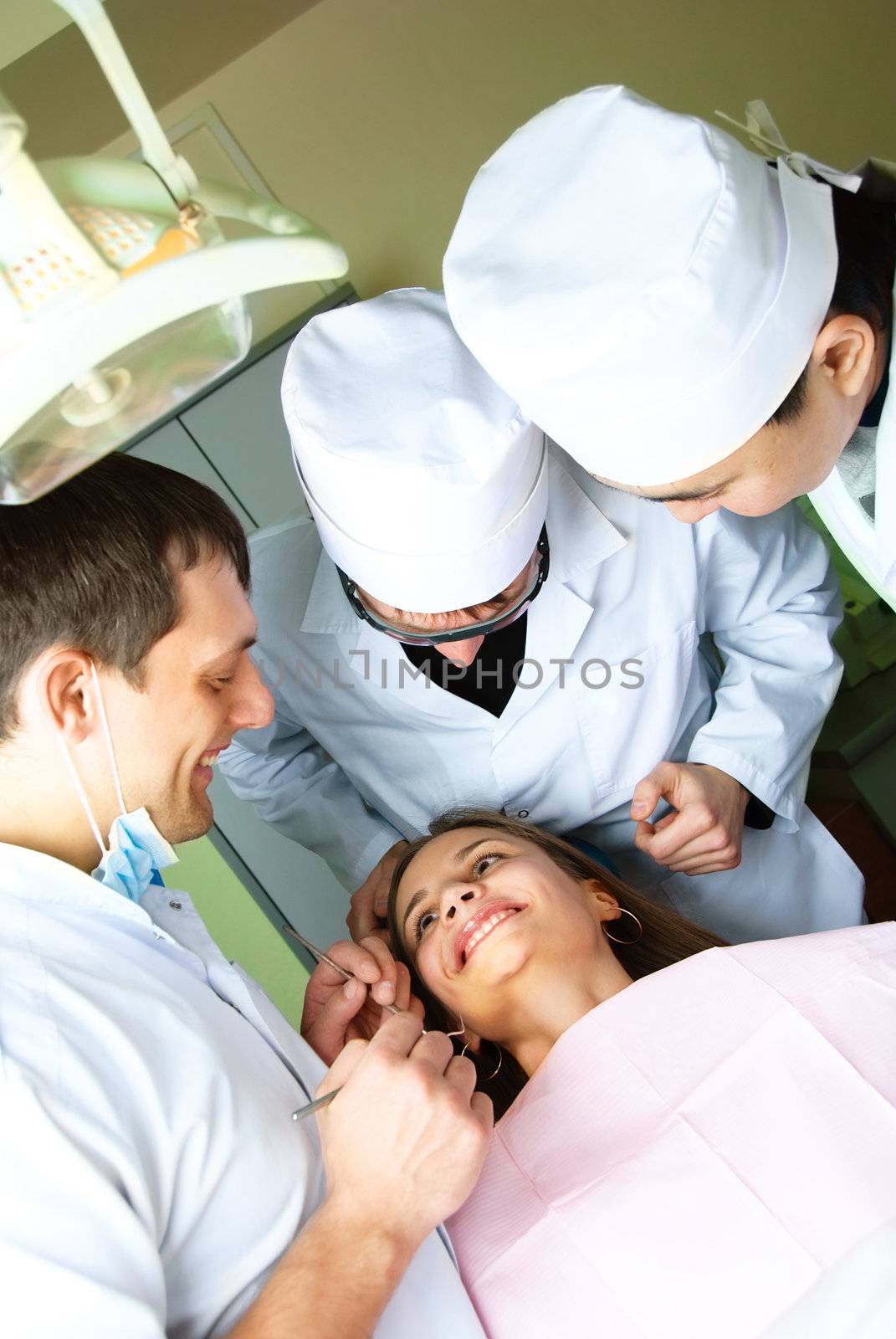 three dentists bend over the patient and examine her teeth