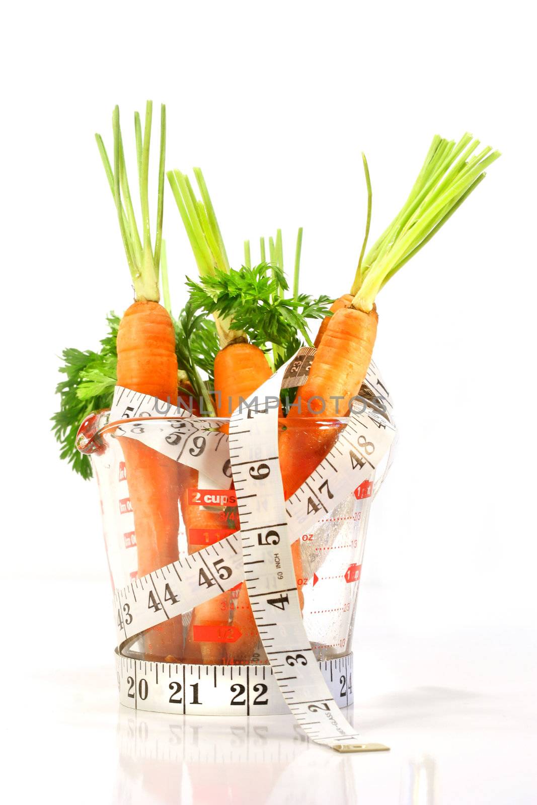 Carrots in a measuring cup with tape measure on white background