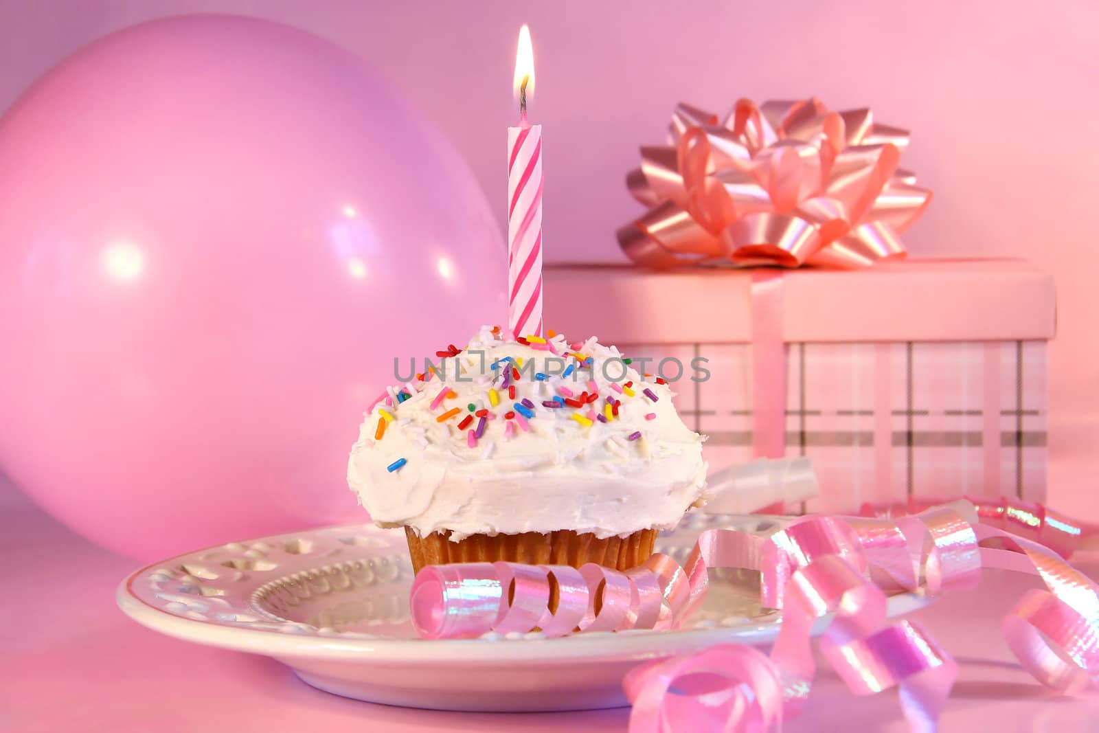 Little cupcake with candle, ballon and gift on pink background