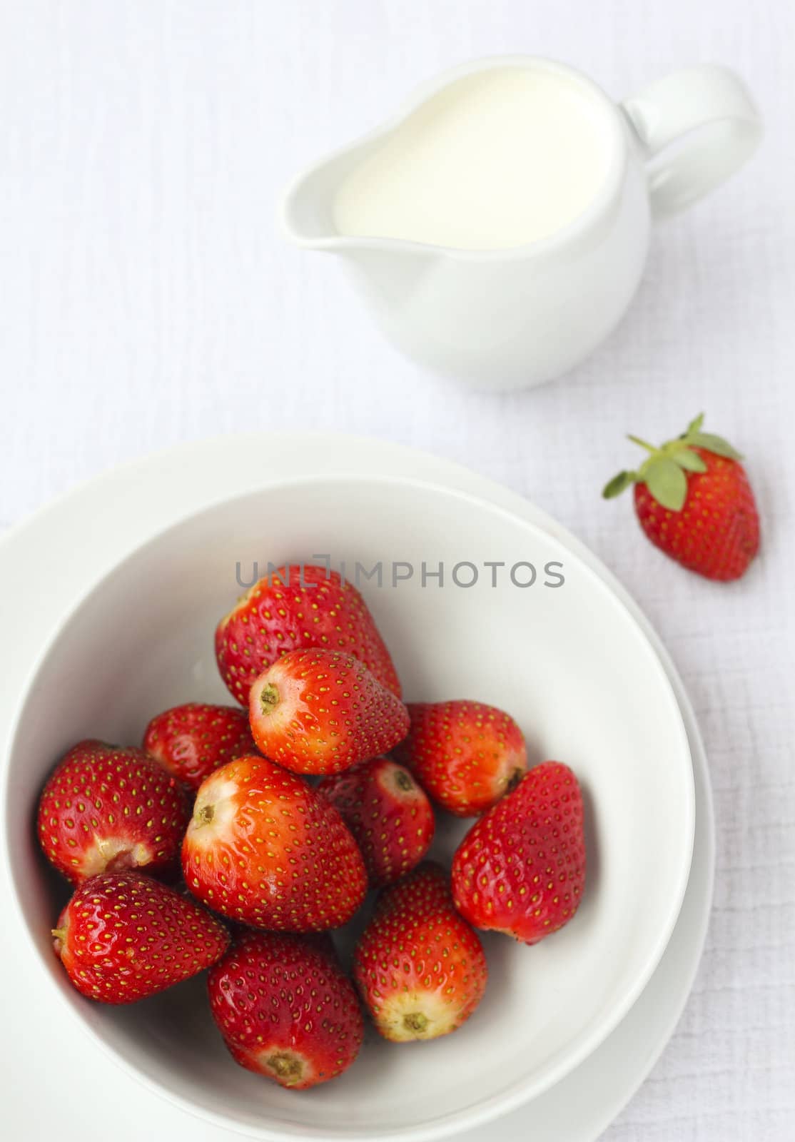 A bowl of ripe strawberries with a jug of cream in the background