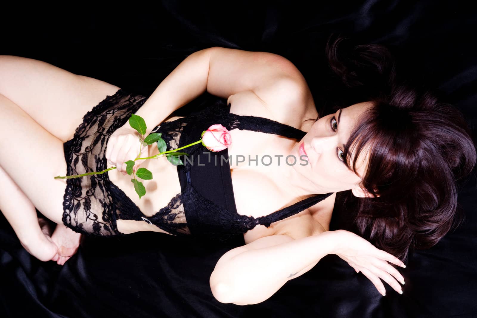 woman lying on a black sheet in lingerie with a single rose