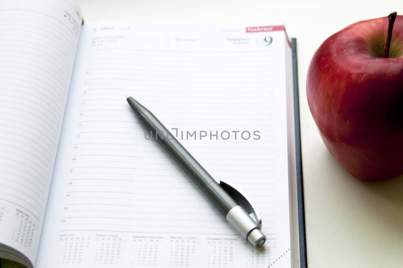 An apple lay near notebook next to pencil