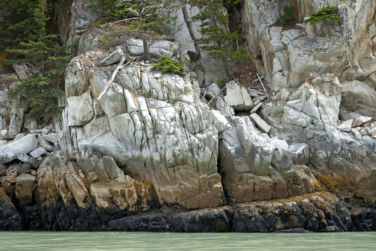 Rocks create a wall of stone in beautiful colors at water's edge by Claudine