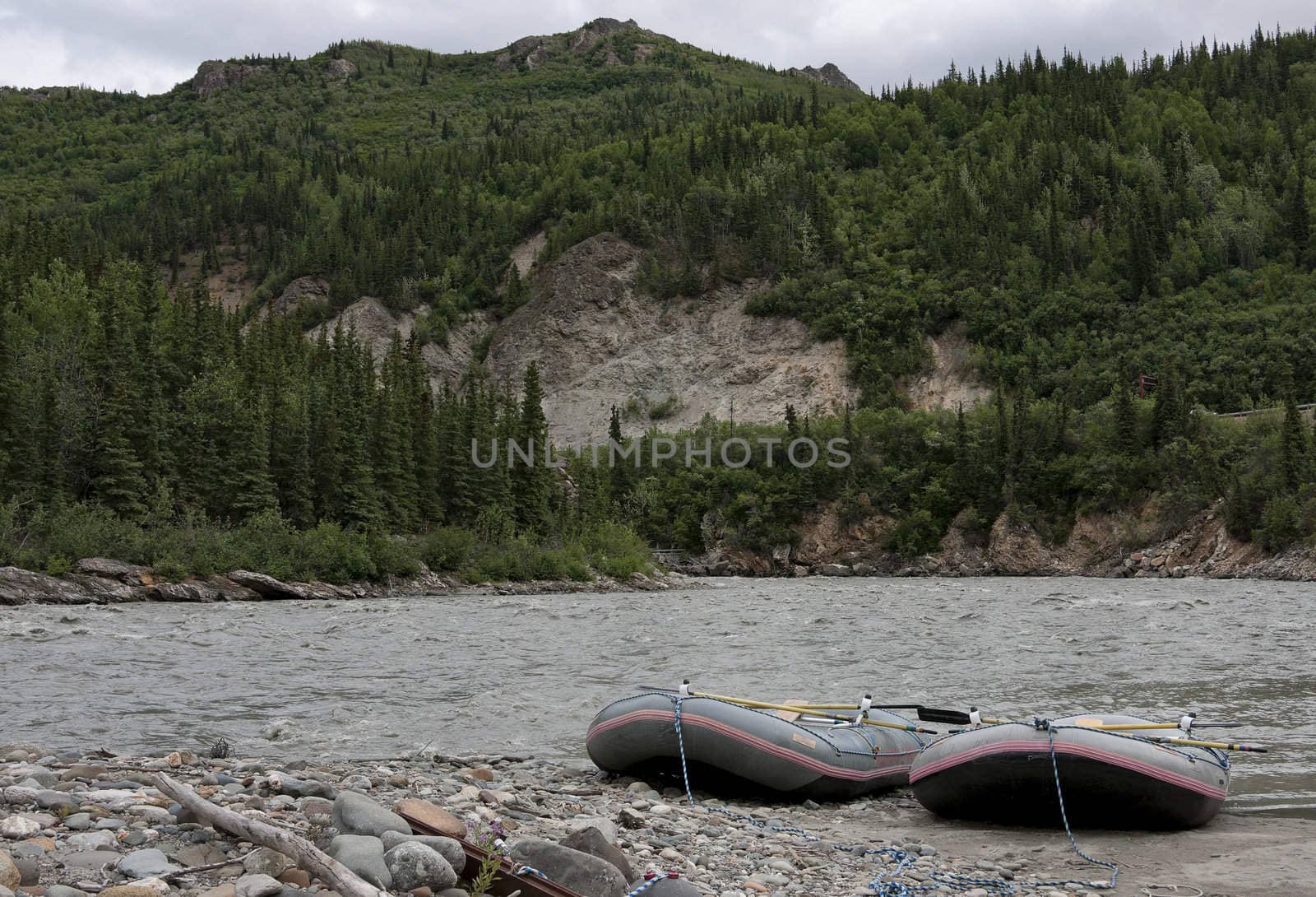 Two boats resting on the shore of a grey wild river.