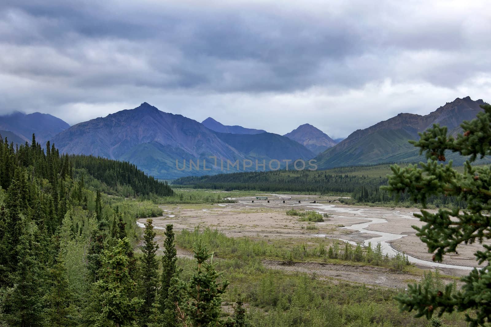 Spectacular wide view over valley with narrow meandering river and mountains in the background.