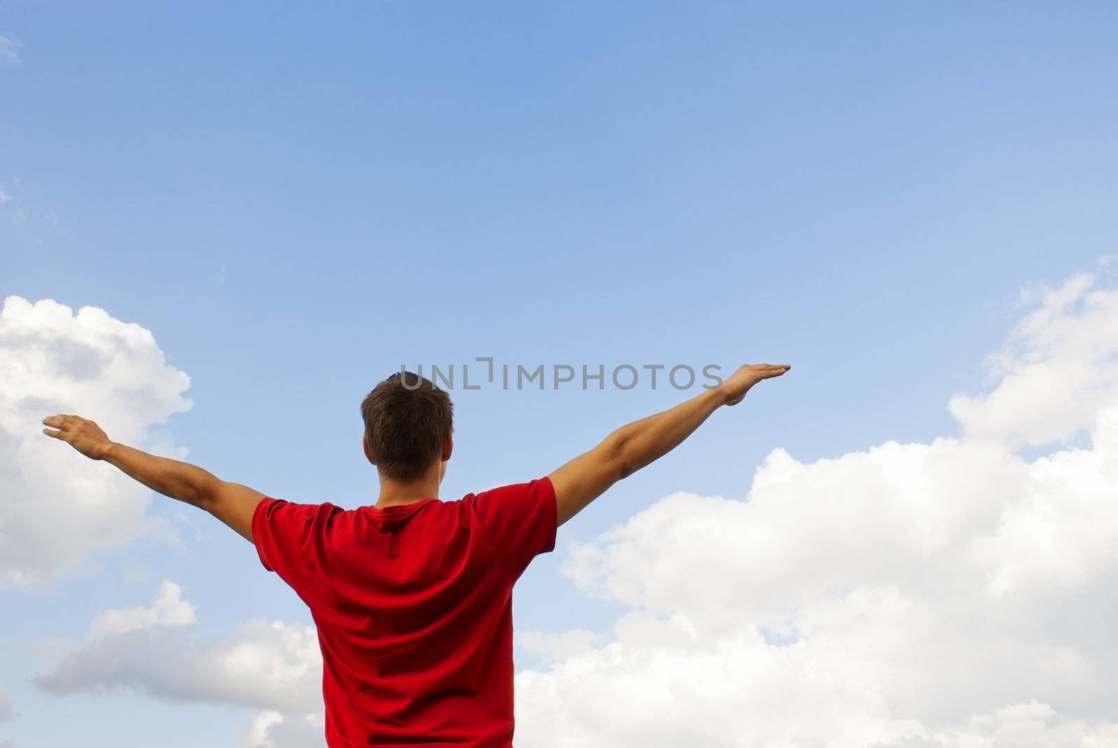 Young man staying with raised hands against blue sky by AndreyKr