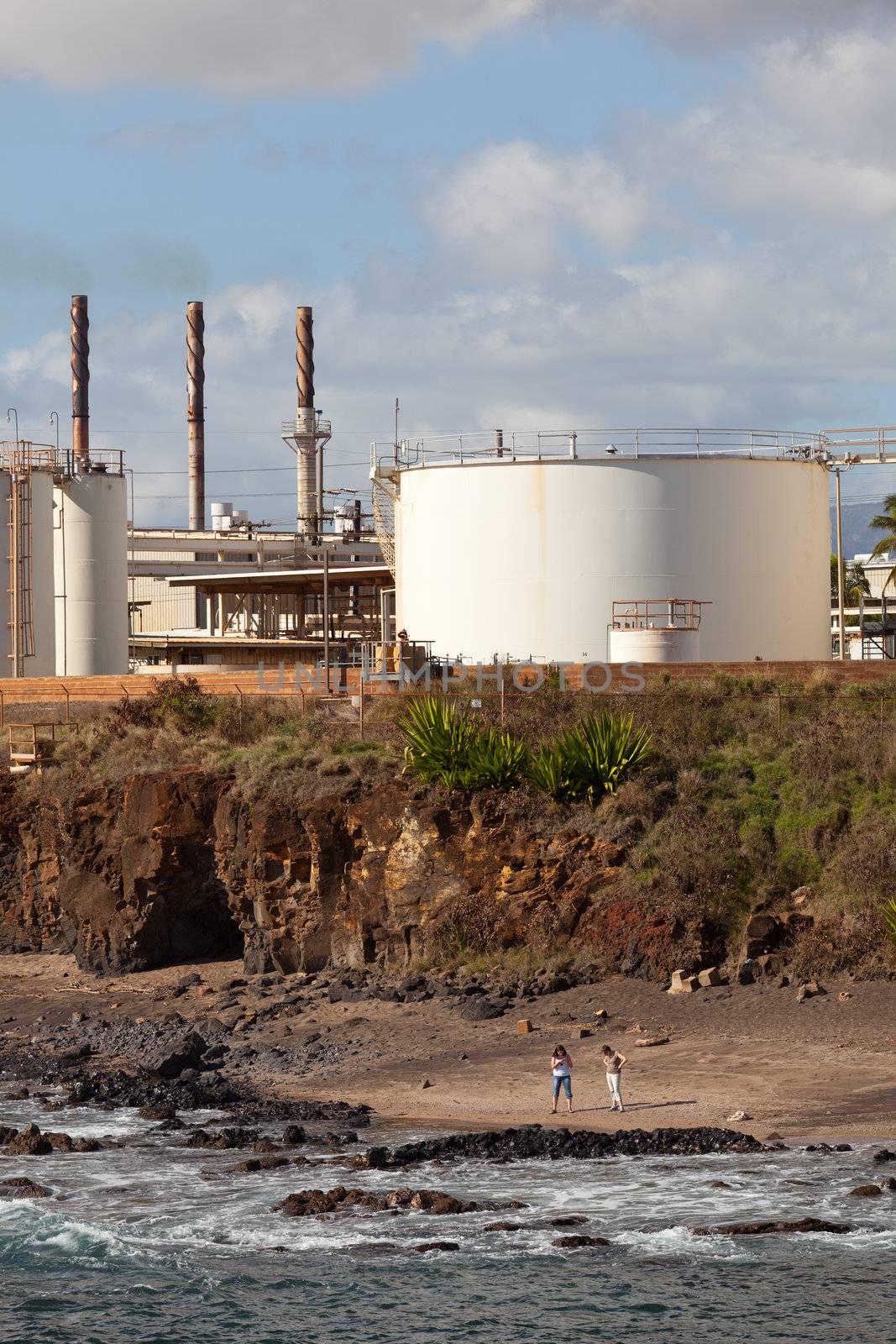 Two women looking on Glass Beach Kauai with refinery behind