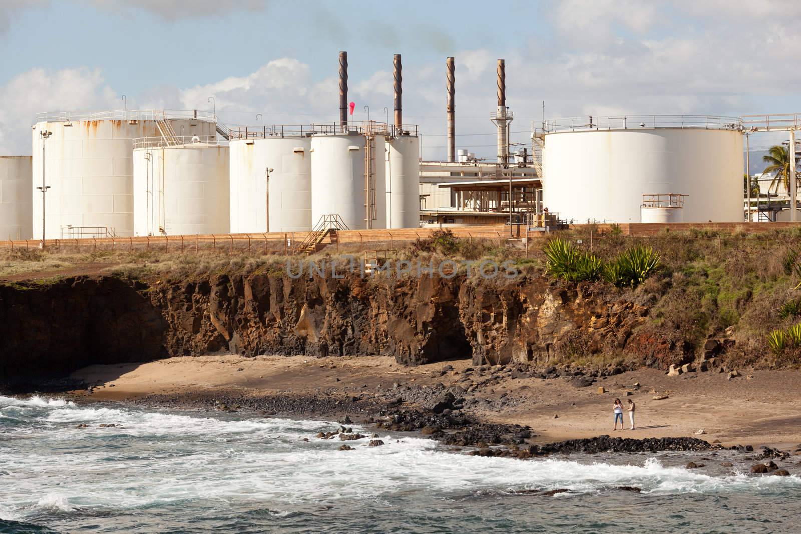 Two women looking on Glass Beach Kauai with refinery behind