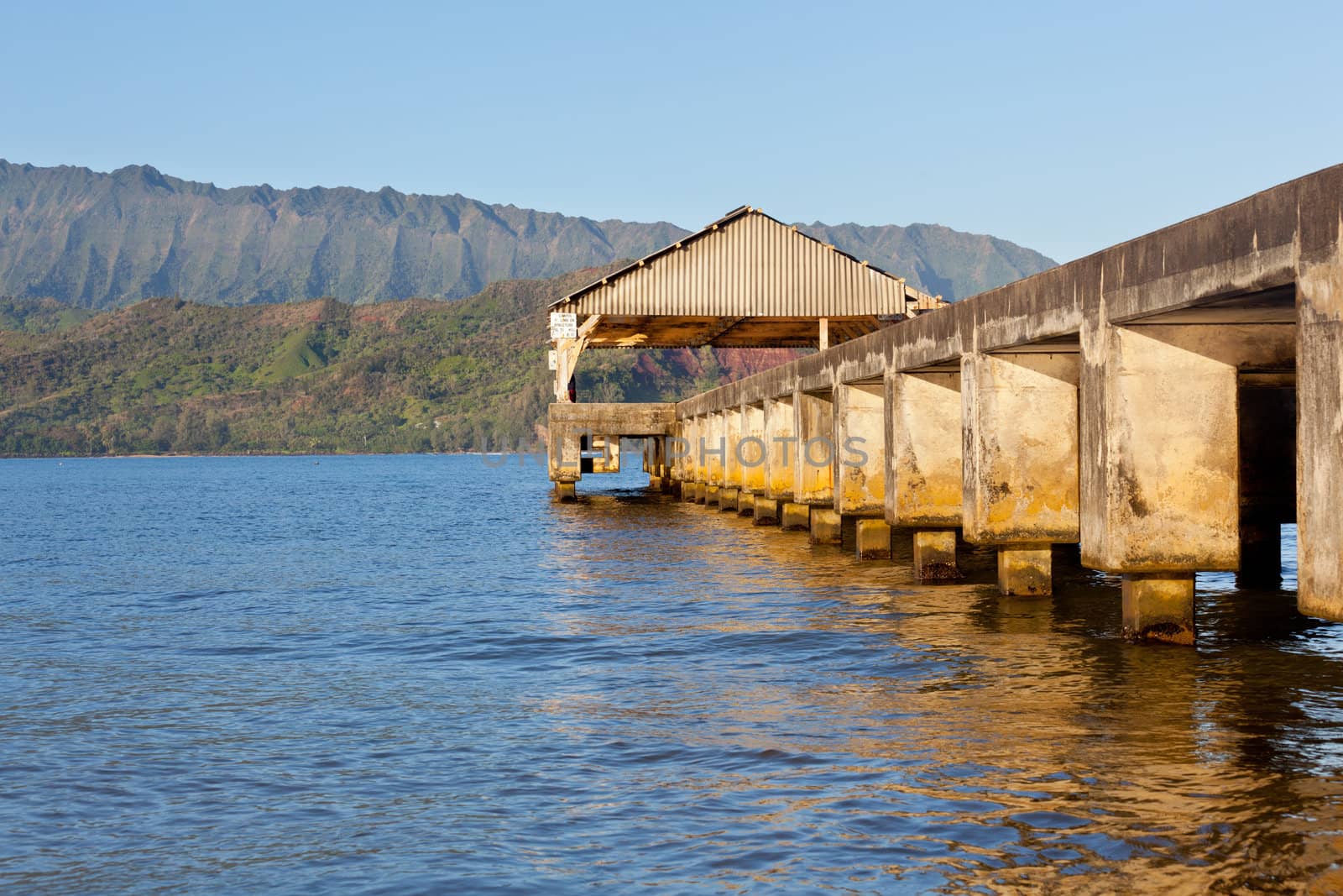 Rising sun illuminates the Hanalei pier and Na Pali mountains in Kauai